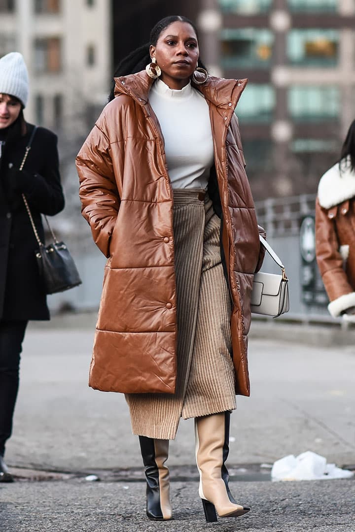 A guest is seen wearing a brown puff coat, white sweater and beige skirt outside the Christopher John Rogers show during New York Fashion Week: A/W20