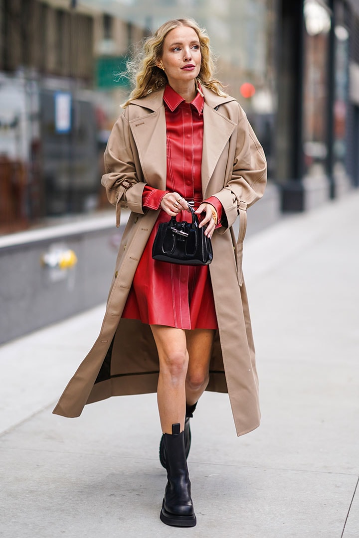 Leonie Hanne wears a light brown trench coat, a red leather dress, black leather boots, a bag, outside Longchamp, during New York Fashion Week Fall-Winter 2020
