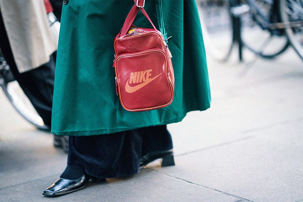 A guest wears a green trench coat, a red Nike travel bag, during London Fashion Week February 2019 on February 15, 2019 in London, England.