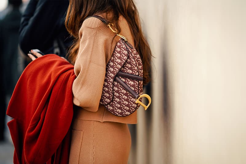 A guest wears a camel suit, a burgundy Dior monogram saddle bag, and holds a red coat, outside Dior, during Paris Fashion Week Womenswear Fall/Winter 2019/2020, on February 26, 2019 in Paris, France.