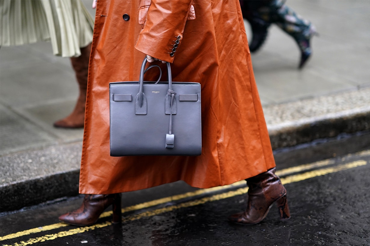 A guest wears an orange bag and a gray Saint Laurent YSL bag, during London Fashion Week Fall Winter 2020 on February 16, 2020 in London, England.