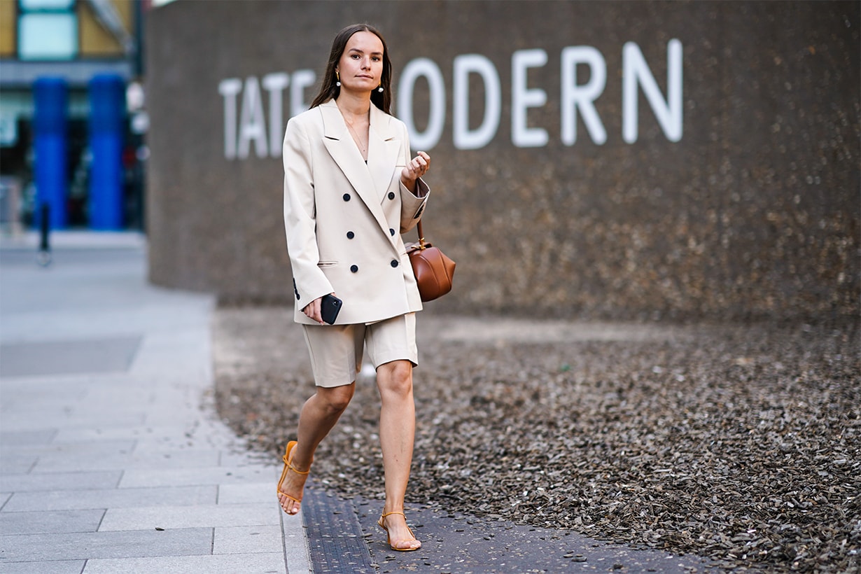 A guest wears earrings, a beige oversized blazer jacket, a brown leather bag, beige shorts, orange shoes, during London Fashion Week September 2019 on September 14, 2019 in London, England. 