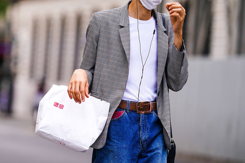 A passerby wears a blazer jacket, a white t-shirt, a brown leather belt, blue jeans, a Uniqlo shopping bag, on July 23, 2020 in Paris, France.