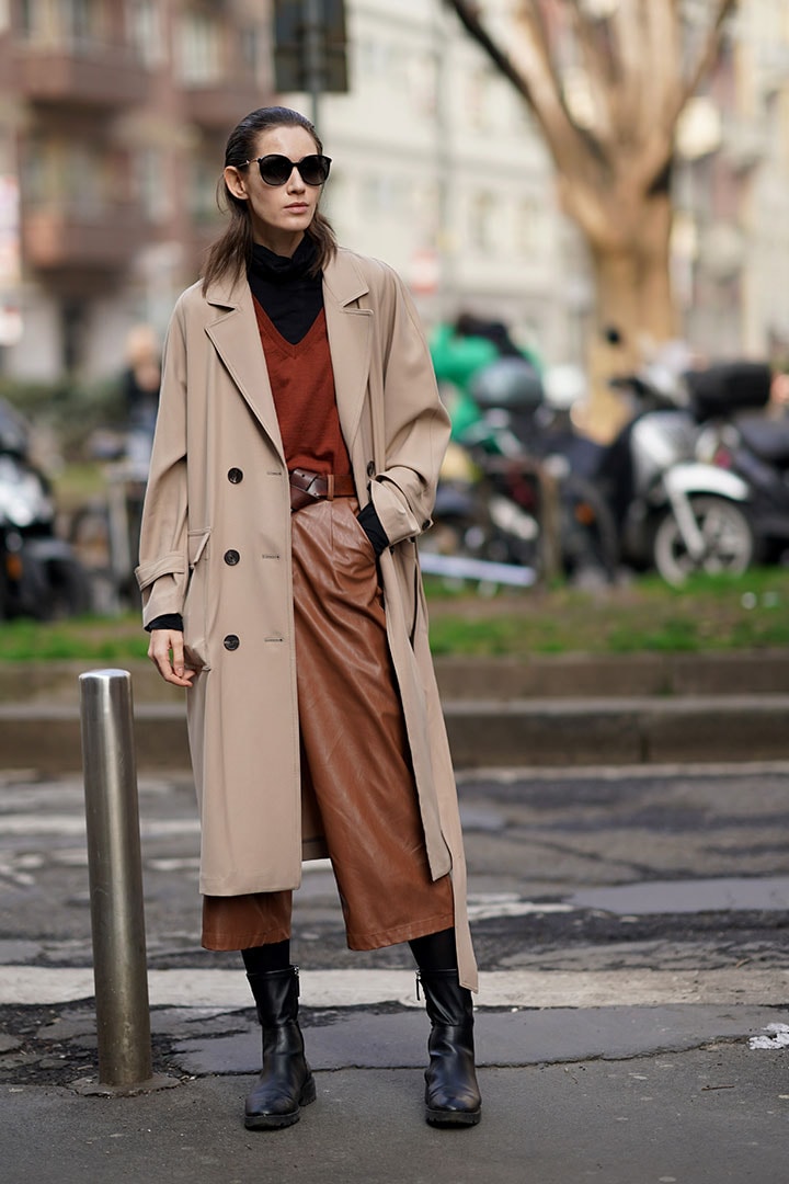 A model wears sunglasses, a beige long coat, a black turtleneck pullover, a brown v-neck pullover, a brown leather belt, brown leather pants, outside Calcaterra, during Milan Fashion Week Fall/Winter 2020-2021, on February 19, 2020 in Milan, Italy.