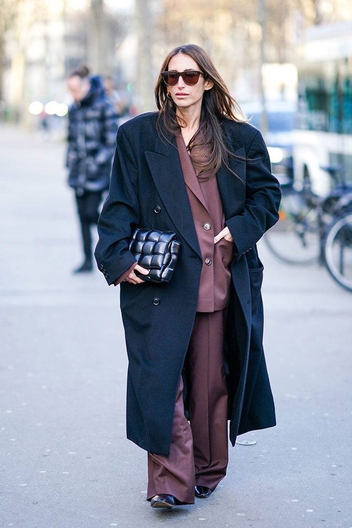 Chloe Harrouche wears sunglasses, a black oversized long coat, a black woven leather quilted Bottega Veneta bag, a brown jacket, flared pants, black leather shoes, outside Schiaparelli, during Paris Fashion Week - Haute Couture Spring/Summer 2020, on January 20, 2020 in Paris, France.