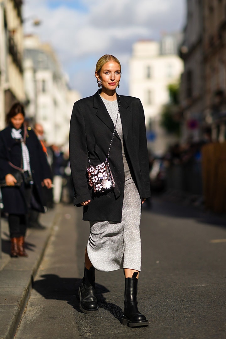 Leonie Hanne wears a black oversized blazer jacket, a grey glitter dress, a silver shiny sequined bag with attached floral designs, black leather boots, outside Paco Rabanne, during Paris Fashion Week - Womenswear Spring Summer 2021, on October 04, 2020 in Paris, France.