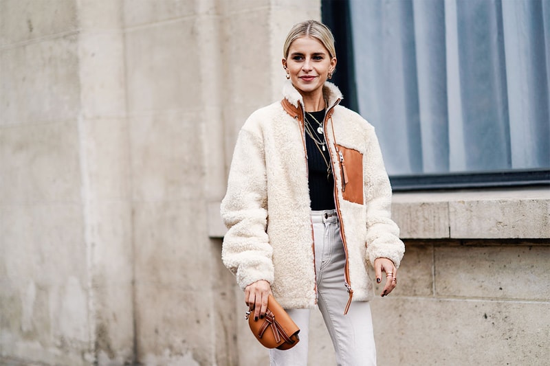 Caroline Daur (L) wears earrings, a black top, a white sheepskin Loewe jacket, a small brown Loewe clutch, white pants, outside Nina Ricci, during Paris Fashion Week Womenswear Fall/Winter 2019/2020, on March 01, 2019 in Paris, France.